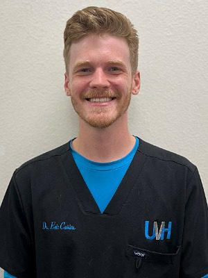 Dr. Eric Collins, male wearing a blue long sleeve shirt under black scrubs